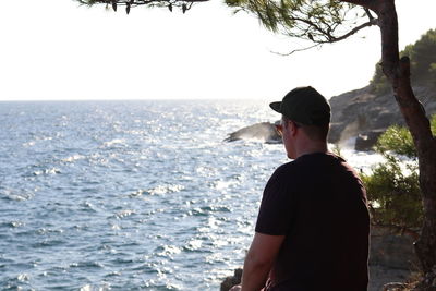 Rear view of man standing by sea against clear sky
