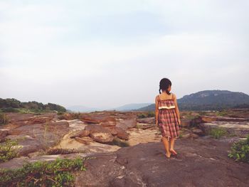 Rear view of girl standing on rock against sky