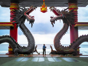 Friends standing amidst dragon statues against sea