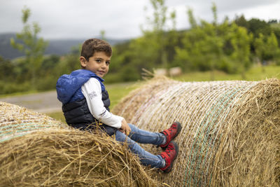Portrait of cute boy sitting on hay bale