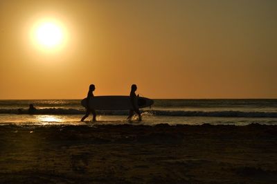 Two silhouette surfers walking on calm beach