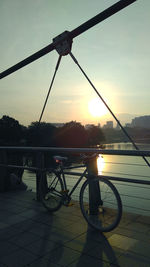 Bicycles on bridge in city against sky during sunset