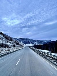 Road by snowcapped mountain against sky during winter