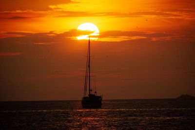 Silhouette sailboat in sea against sky during sunset