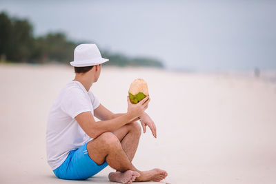 Full length of man holding chocolate while sitting on beach