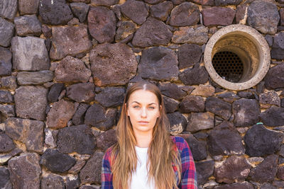 Portrait of young woman standing against stone wall