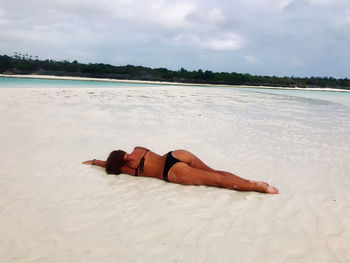 Woman lying down on land against sky