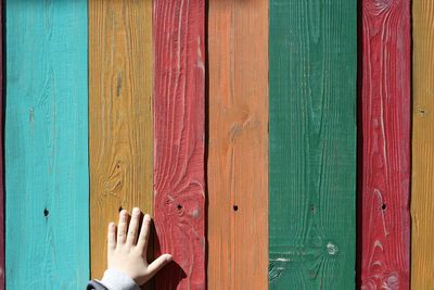 Cropped hand of child touching colorful painted wooden wall