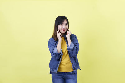 Portrait of beautiful young woman standing against yellow background