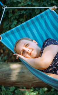 A girl with blond hair and in a dress lies in a hammock outdoors on a sunny summer day