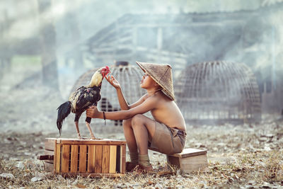 Boy looking at rooster while sitting outdoors