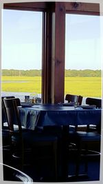 Empty chairs and tables against sky seen through window