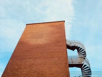 Low angle view of  brick wall building with spiral staircase of fire escape against sky