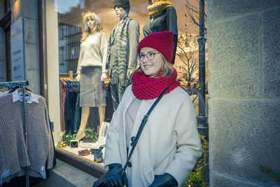 Smiling woman looking away while standing by clothing store