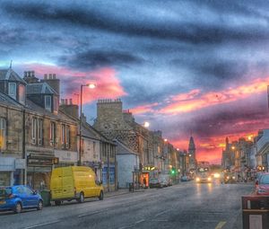 Vehicles on road against buildings at sunset