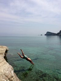 Shirtless man diving into sea against sky