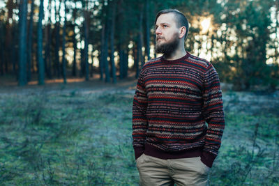Thoughtful man standing with hands in pockets at forest