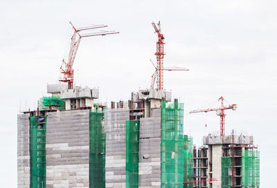 Low angle view of crane by building against sky