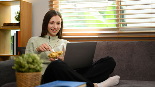 Portrait of young woman using laptop while sitting on sofa at home