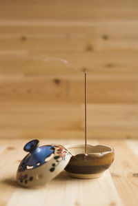 Burning incense stick on container against wooden wall