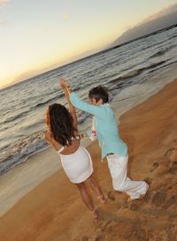 Rear view of friends enjoying at beach against sky