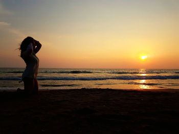 Woman standing on beach against sky during sunset