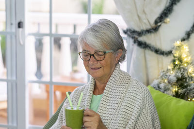Smiling senior woman holding juice sitting at home