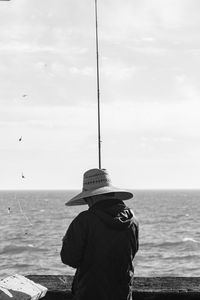 Rear view of man fishing at sea against sky