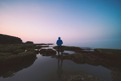 Rear view of man looking at sea against sky during sunset