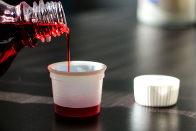 Close-up of bottle pouring cough syrup in container on table