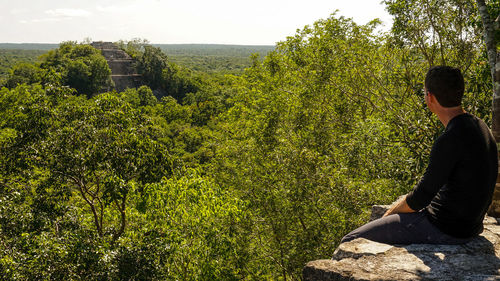 Young man sitting on rock against trees