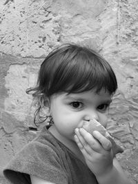 Portrait of girl eating bread while sitting against wall