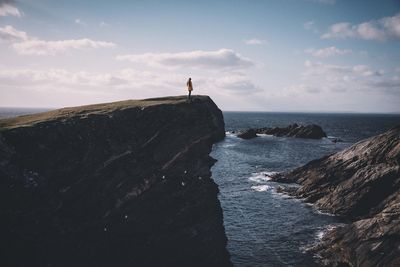 Woman standing on rocky shore against the sky