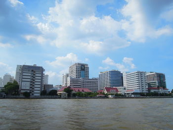 City at waterfront against cloudy sky