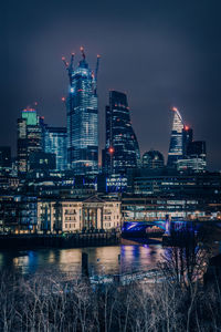 Illuminated buildings by river against sky at night