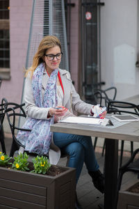 Woman writing on paper while sitting at sidewalk cafe