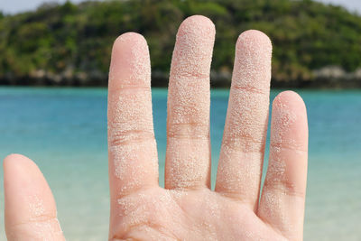 Cropped image of kid hand with sand against sea