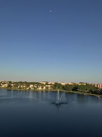 City by lake against clear blue sky