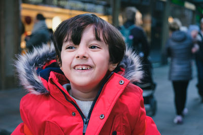 Portrait of cute 4 years old boy with brown hair and red jacket outdoors in the city 