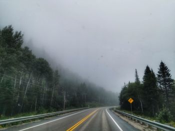 Country road by trees against sky during rainy season