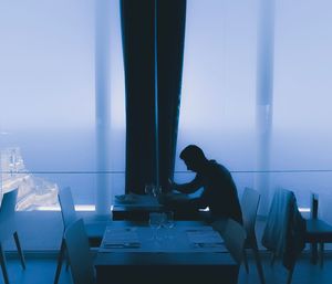 Young man eating food while sitting at table by window in restaurant