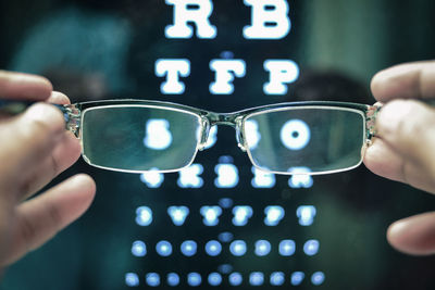 Cropped hands holding eyeglasses against alphabets