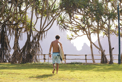 Young man walking and carrying surfboard