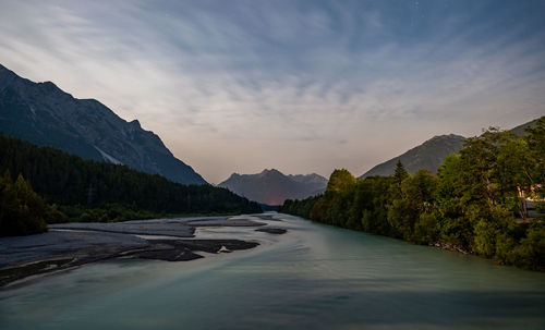 Scenic view of river amidst mountains against sky at sunset
