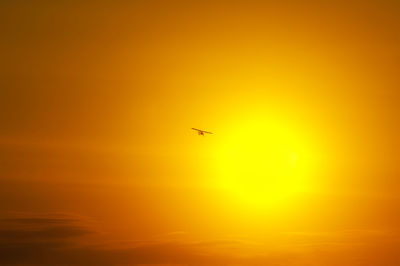 Low angle view of silhouette airplane flying against orange sky