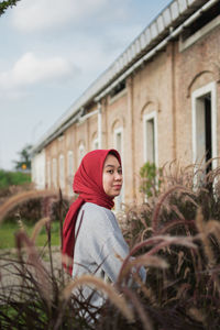 Portrait of young woman standing against building