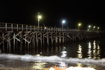 Illuminated bridge over river against sky at night