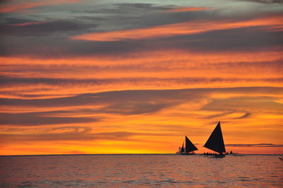 Sailboat sailing on sea against orange sky