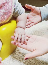 Cropped hands of mother and daughter touching baby at home