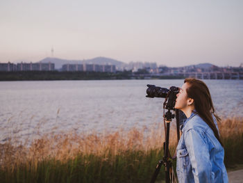 Woman photographing against sky during sunset